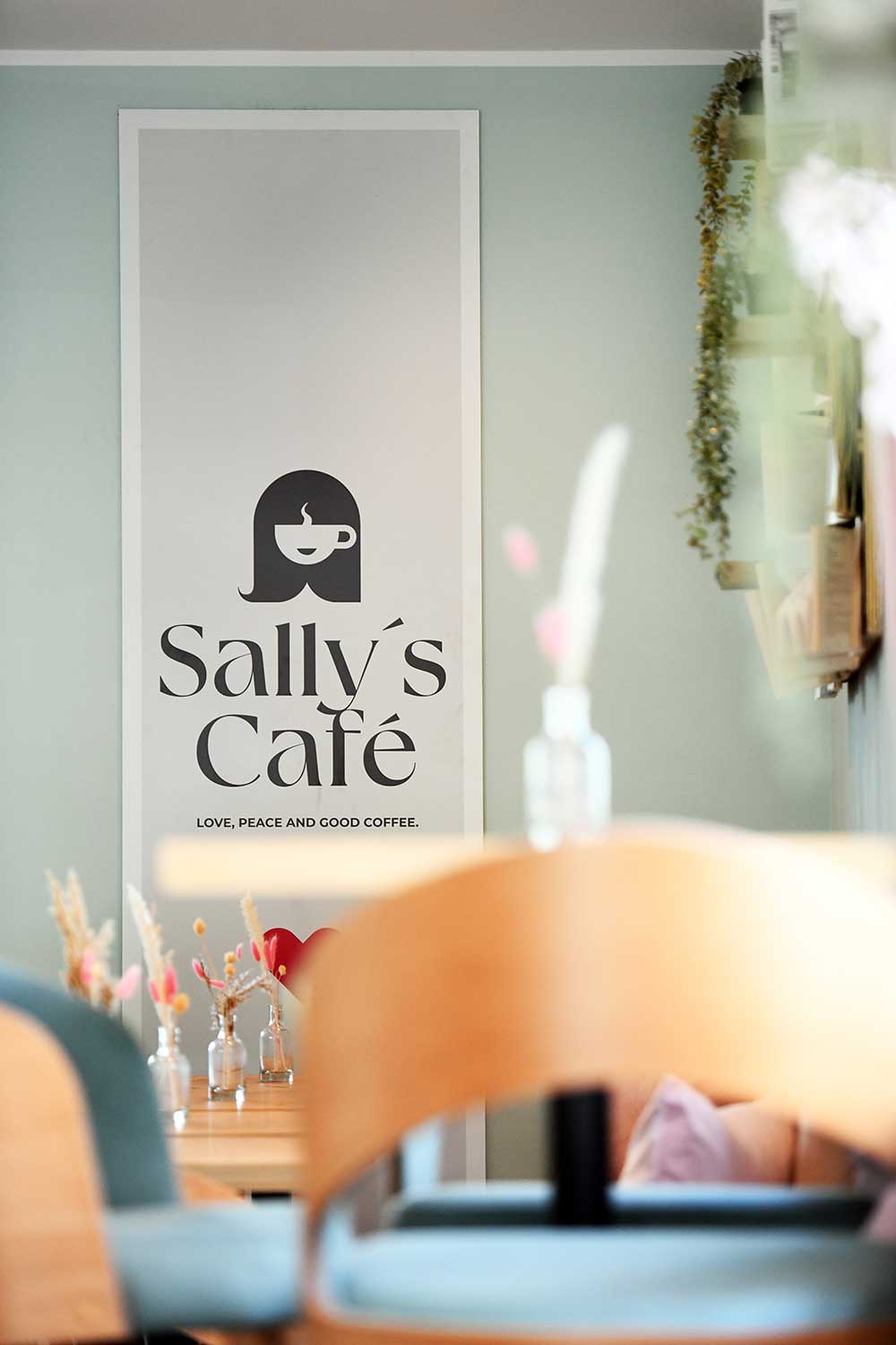 Wand im Café mit dekorativem Poster von 'Sally's Cafe', umgeben von stilvoller Deko, die das gemütliche Ambiente des Cafés unterstreicht.
